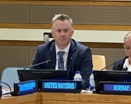 George Willcoxon seated behind the United Nations nameplate at the Ad Hoc Liaison Committee meeting in New York